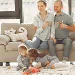 Cheerful family smiling while spending weekend together sitting parents sitting on comfortable sofa while children resting on carpet and playing